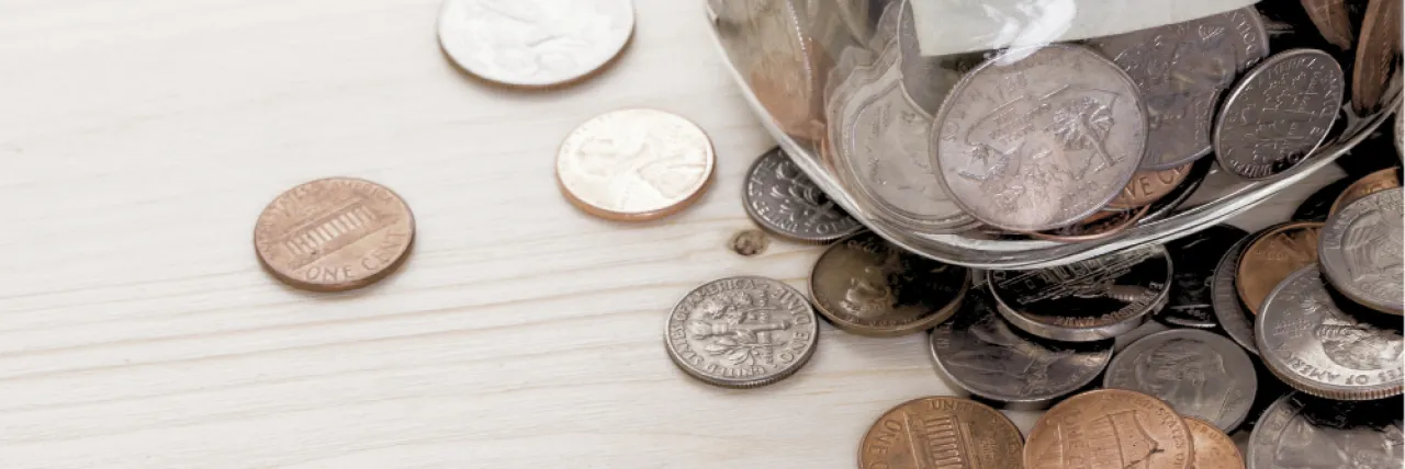 coins strewn across a table underneath a jar full of coins