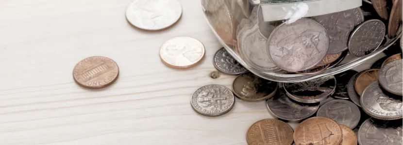 coins strewn across a table underneath a jar full of coins