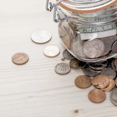 coins strewn across a table underneath a jar full of coins